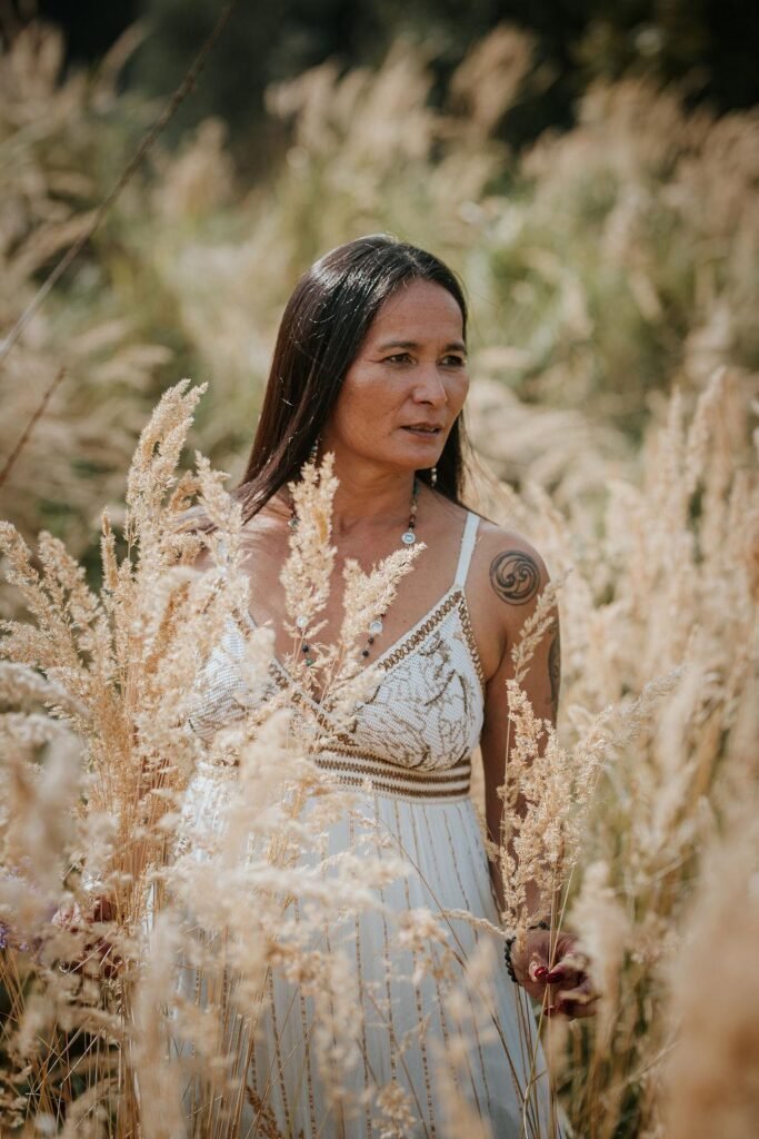 Vrouw in witte jurk loopt tussen goudkleurige grassen in het zonlicht, symbool voor vrijheid, zachtheid en verbinding met de natuur – sfeerbeeld van Ancestral Earth.