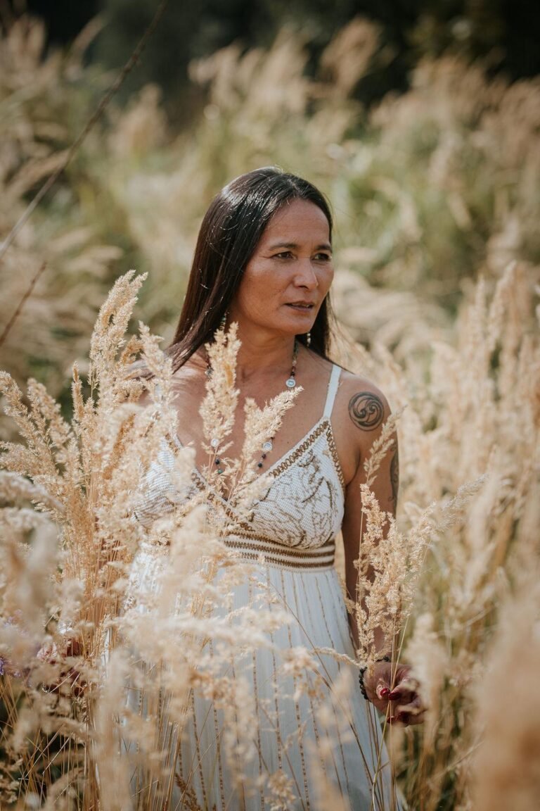 Vrouw in witte jurk loopt tussen goudkleurige grassen in het zonlicht, symbool voor vrijheid, zachtheid en verbinding met de natuur – sfeerbeeld van Ancestral Earth.